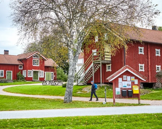 Vandrare på en grusväg vid röda byggnader.