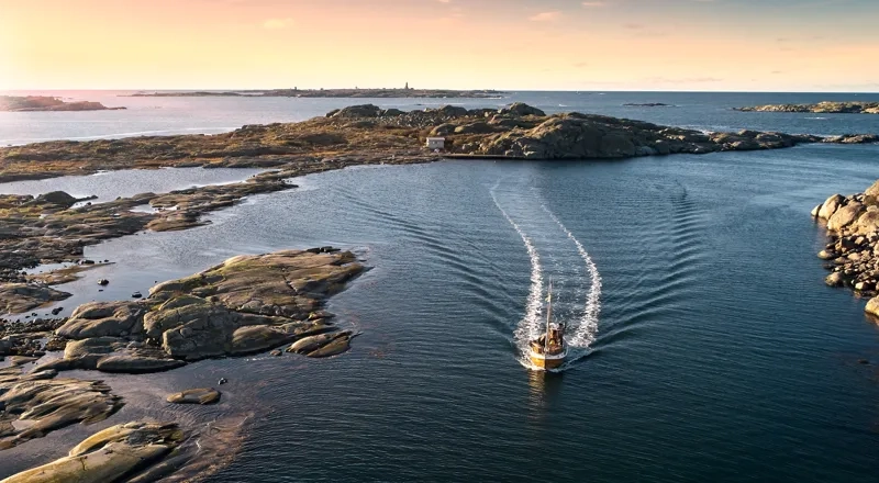 A boat traveling through the water near a rocky shore.