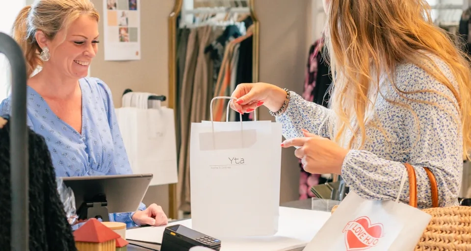 En kvinna handlar och håller i en kasse som det står "I Love Hjo" på, och kassörskan ler