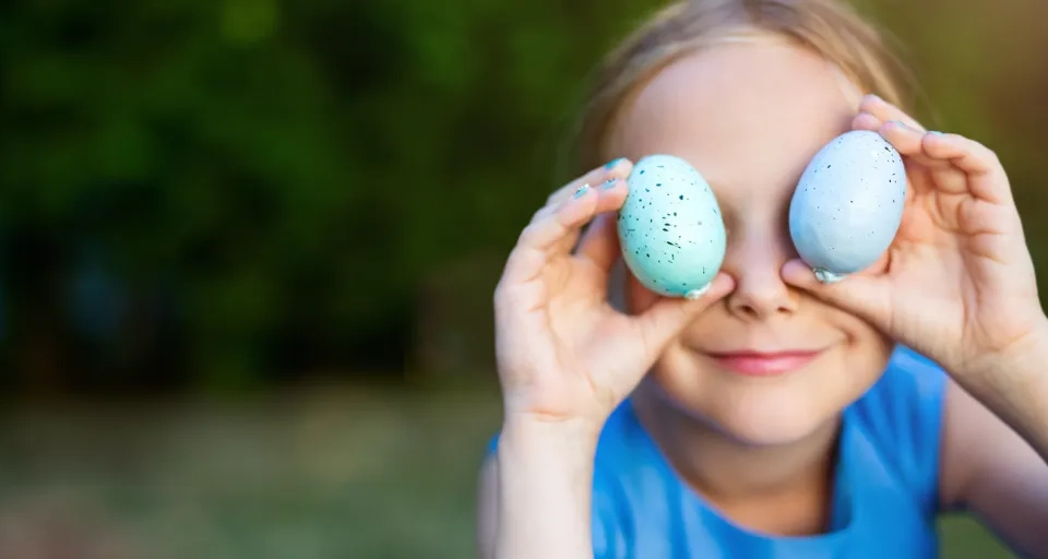 Flicka håller två naturfärgade ägg för ögonen och ser finurlig ut.