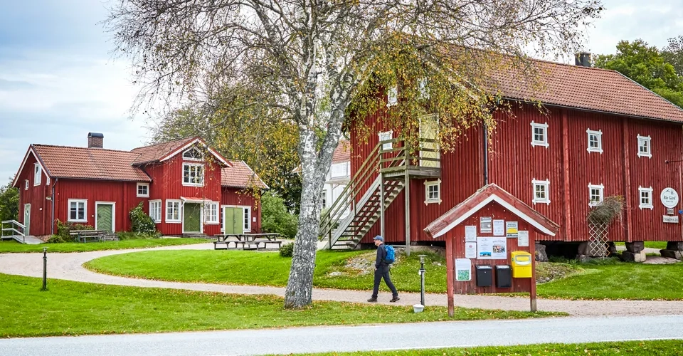 Vandrare på en grusväg vid röda byggnader.