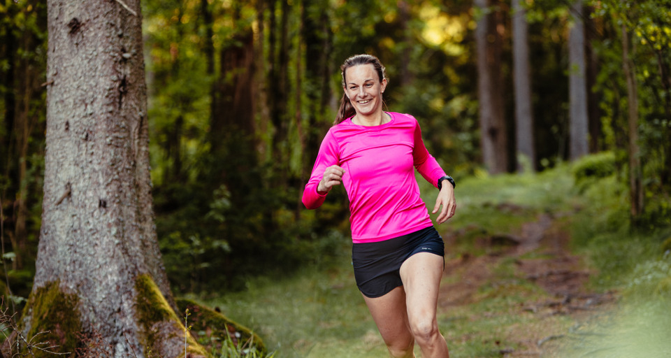 En kvinna i rosa tröja springer i skogen.