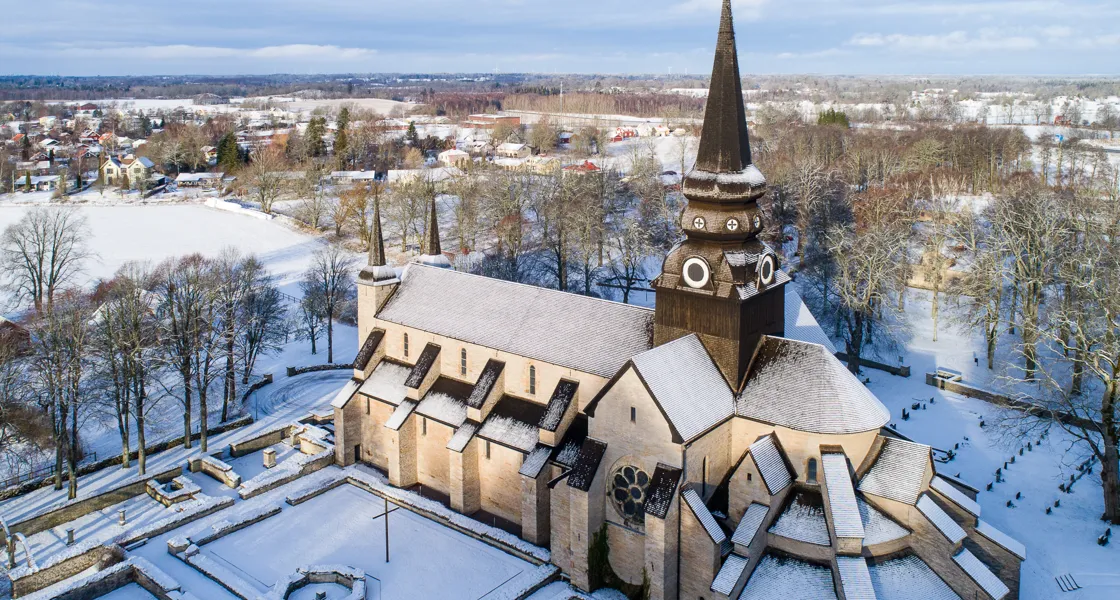 Drönarbild över Varnhems klosterkyrka med snö på taket och det omkringliggande landskapet.