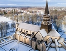 Drönarbild över Varnhems klosterkyrka med snö på taket och det omkringliggande landskapet.