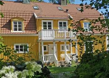 Ett gult hus omgivet av grönska och träd.