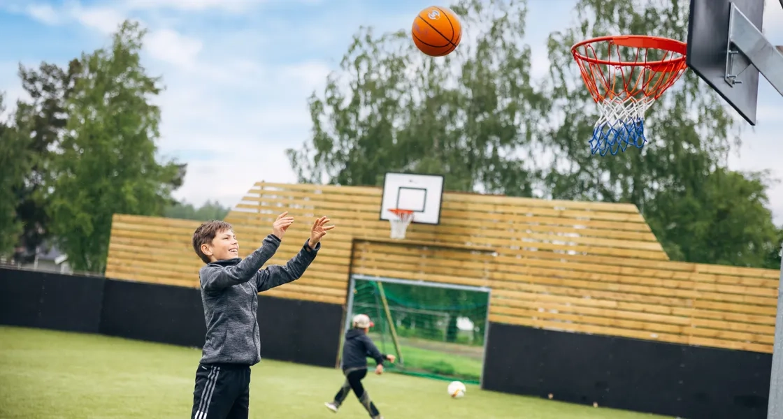 Barn som aktiverar sig med basketboll i ett naturområde.