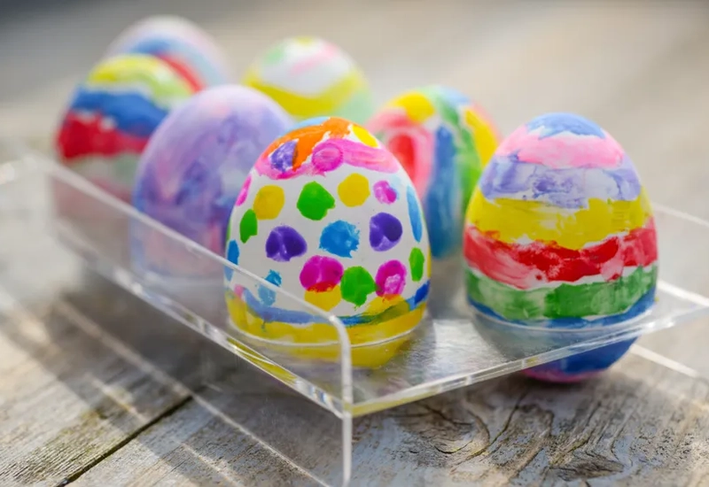 En plastbehållare fylld med målade ägg på ett träbord.