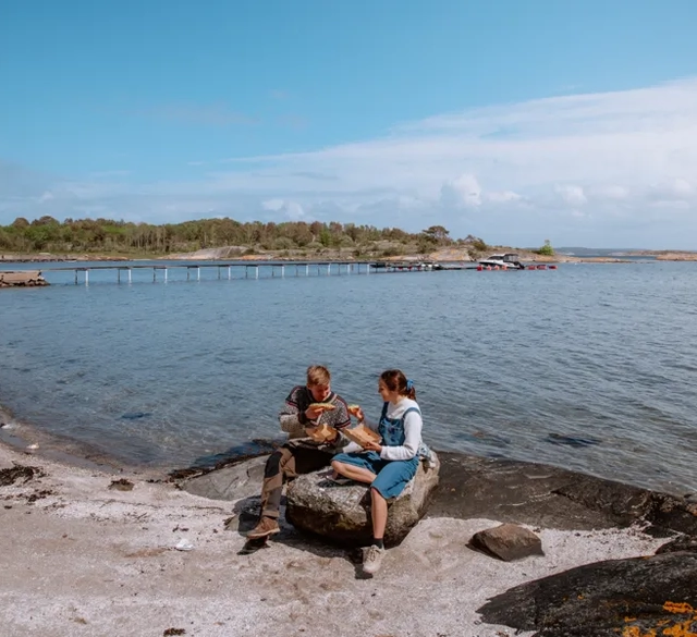 A couple of people sitting on top of a rock next to the sea. 