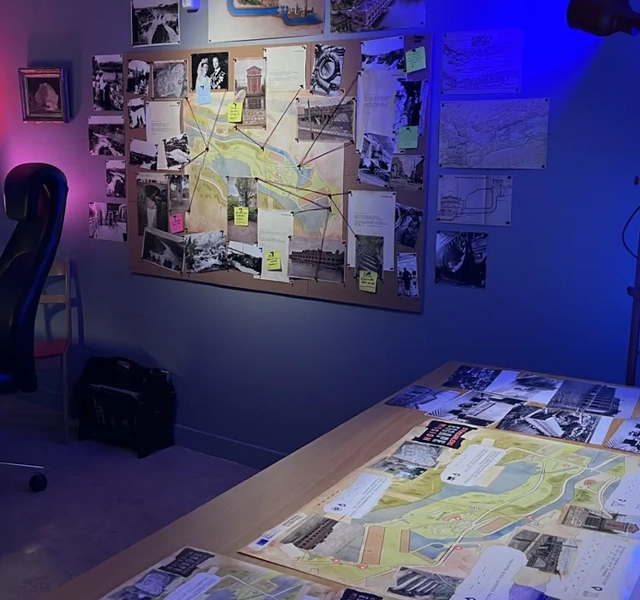 Ett rum med ett skrivbord, en stol, en lampa och tavlor på väggen.