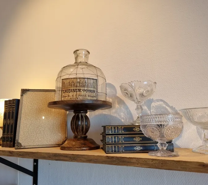 A shelf with a glass jar and other glassware on it.