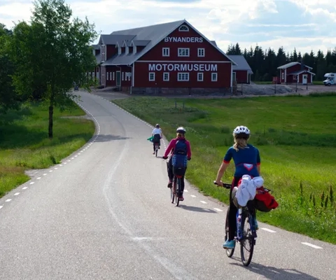 Personer cyklar på landsväg mot en stor röd byggnad