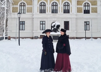 Bild på utsidan av Vänersborgs museum omgivet av snö med två personer som är utklädda i 1800-talskläder