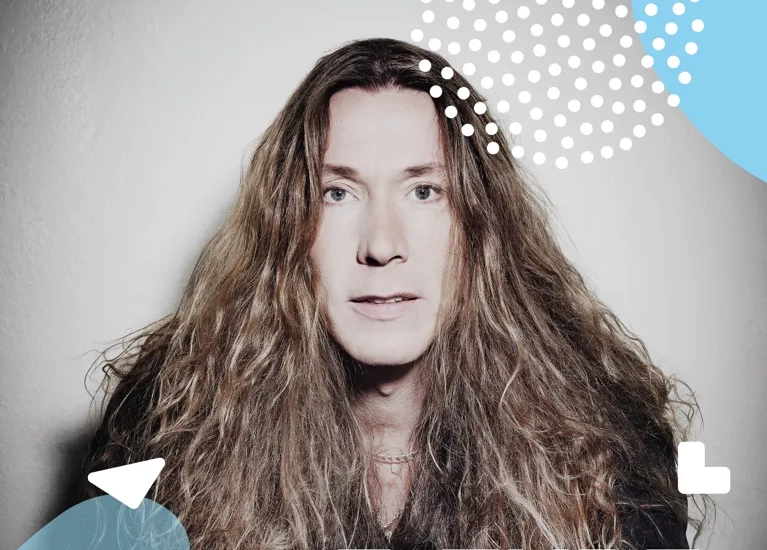 En man med långt hår står framför en vägg.