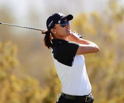 En kvinna som svingar en golfklubba på en golfbana.