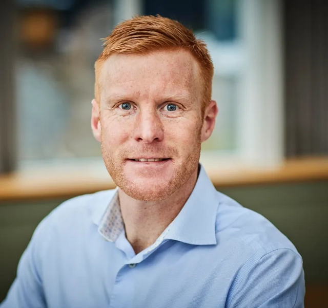 En man med rött hår och blå skjorta.