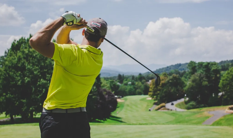 En bild på ryggen av en man som svingar med en golfklubba på en golfbana.