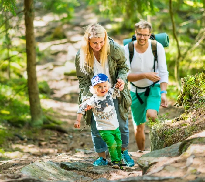 En glad familj som går uppför en backe i en grön skog.