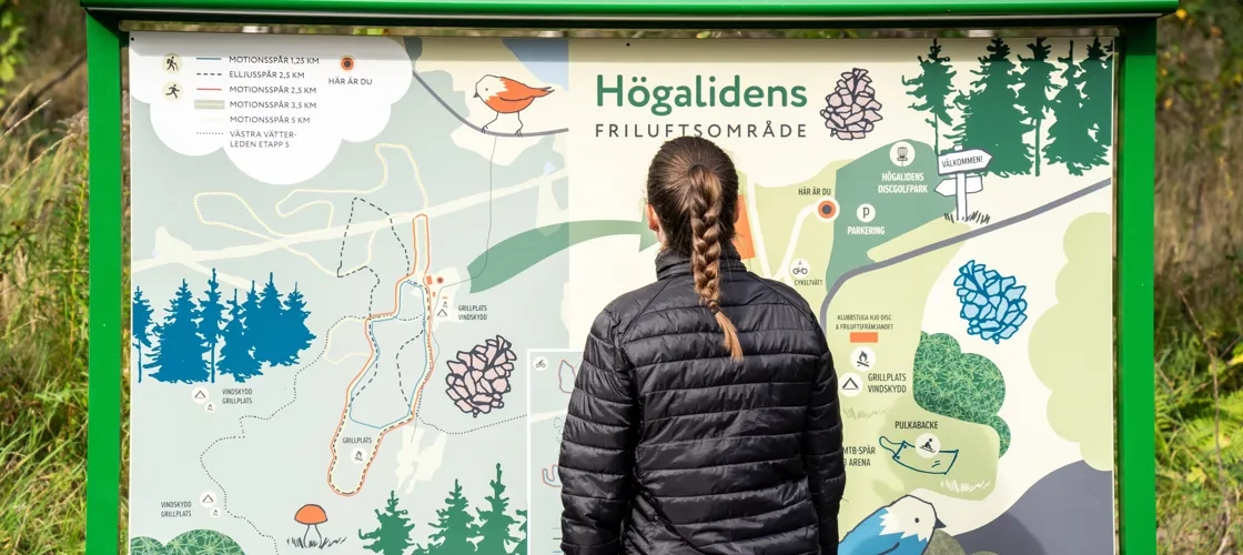 En kvinna som tittar på en skylt med en karta över Högalidens friluftsområde