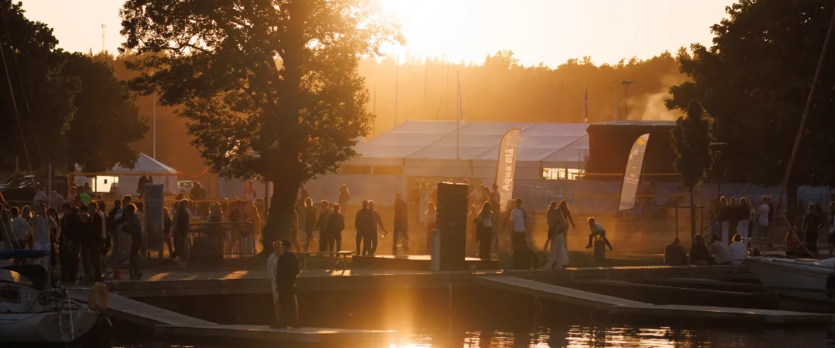 Solnedgång vid ett festivalområde med människor och tält