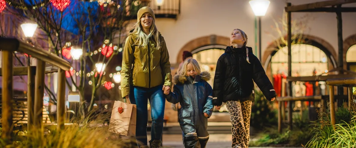En kvinna och två barn går på torget med en shoppingkasse