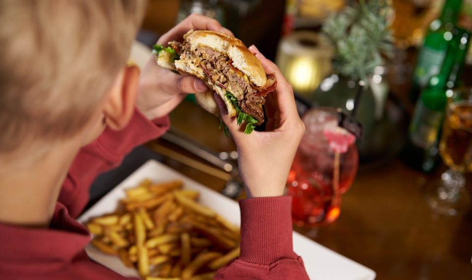 En person som sitter vid ett bord och äter en hamburgare och pommes frites.