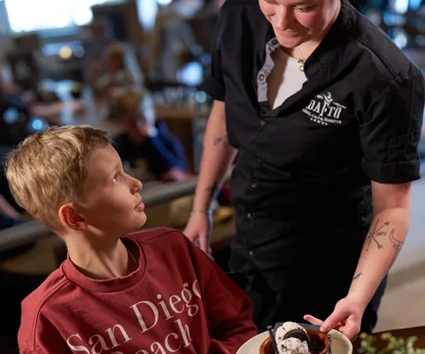 En kvinna serverar en pojke en tallrik med mat.