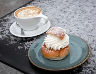 En semla på en tallrik bredvid en kopp kaffe.