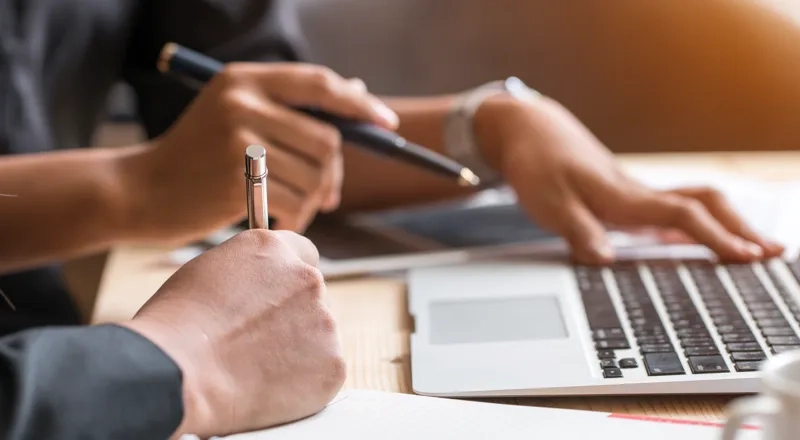 Två personer har ett arbetsmöte med dator och papper.