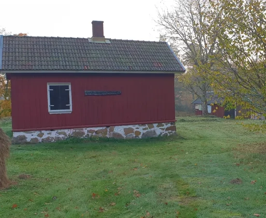 Ett litet rött hus som ligger på ett grönskande fält.
