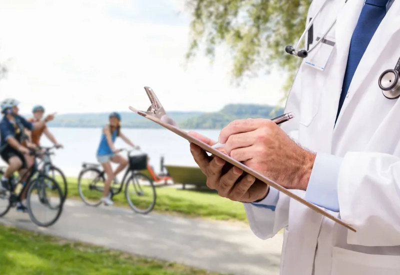 En man i vit labbrock skriver på en skrivplatta med cyklister i bakgrunden.
