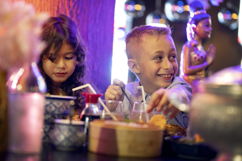 Two children eating at a restaurant with purple-toned surroundings.
