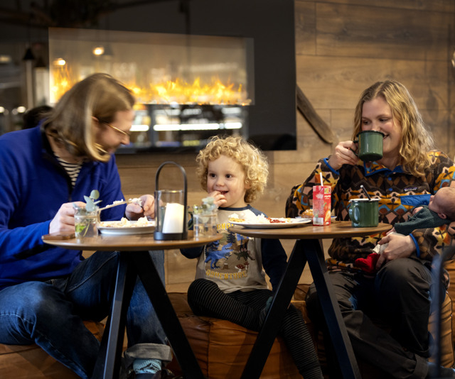 A family sitting and eating at two small tables indoors.