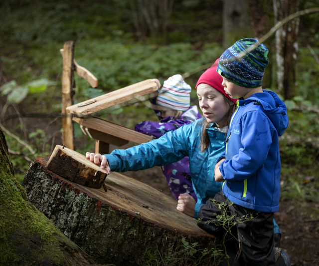 A woman with two children reads a sign in the forest.
