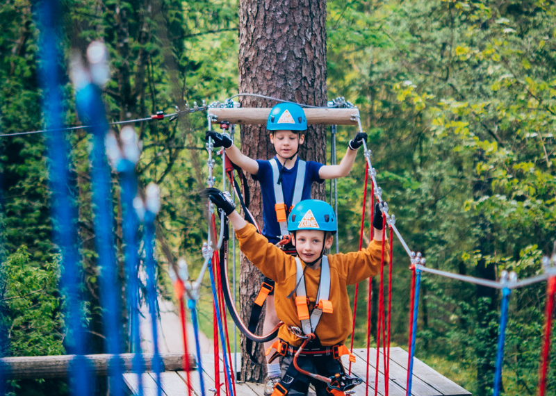 Two boys climbing on an aerial ropes course in the trees.