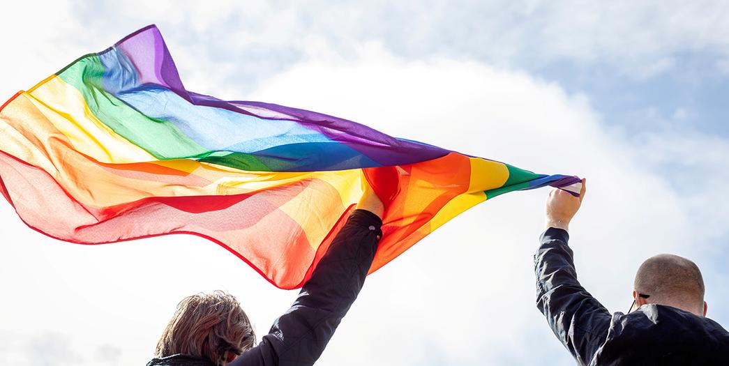 Uppsträckta händer som håller en regnbågsflagga.