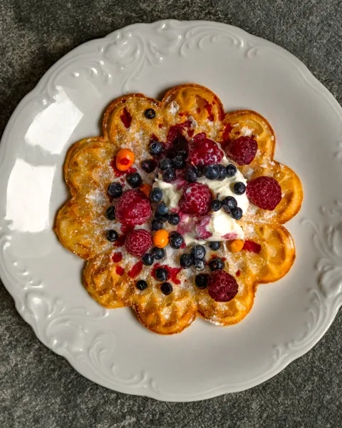 En vit tallrik toppad med våfflor täckta med frukt.