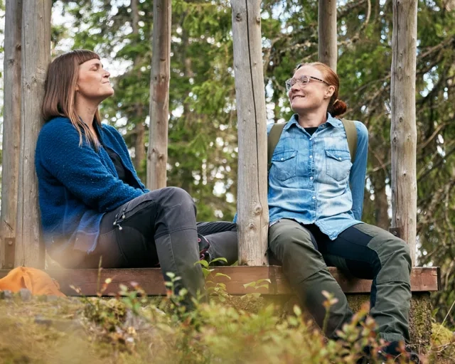 Two people sitting on a bench in the woods.