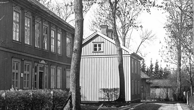 Kullerstensgata med träd på sidan av gatan. På vänstersida av gatan står två hus efter varandra.