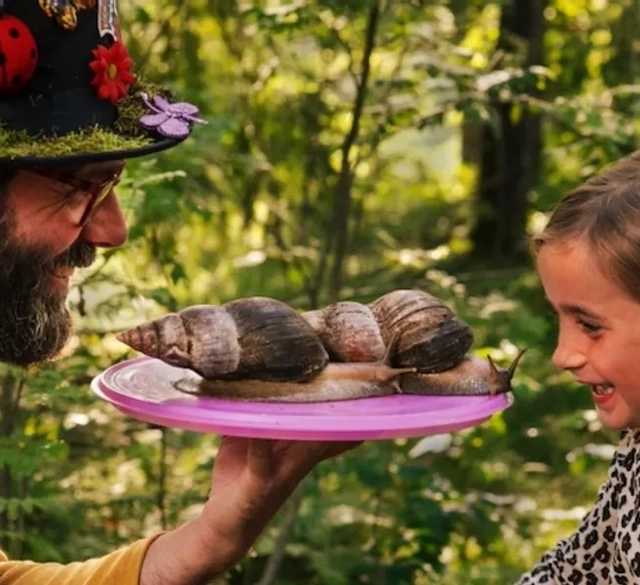 Foto på Kapten Kryp och ett barn som blivit förtjust i jättelandsnäckorna Herman och Afrodite