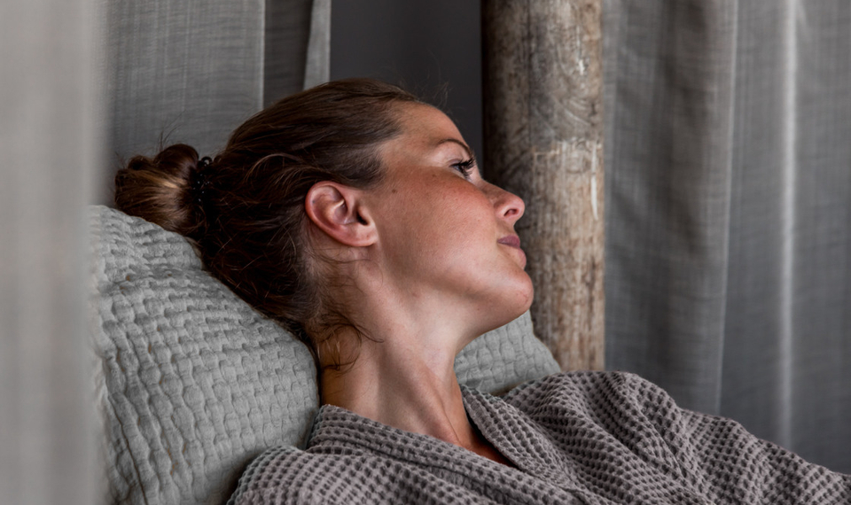 Kvinna med uppsatt hår och iklädd badrock, lutar sig tillbaka och tittar bort från kameran