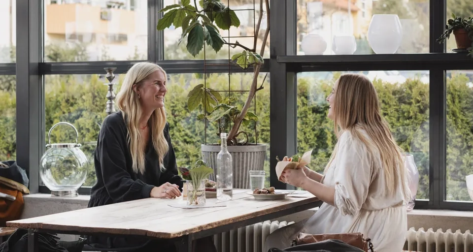 Två kvinnor sitter vid ett bord och pratar med varandra.