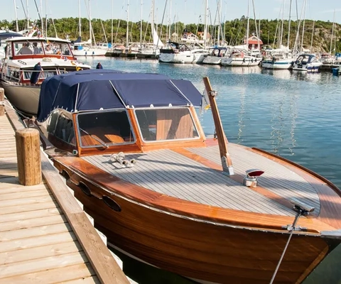En träbåt som ligger vid en brygga med andra båtar.