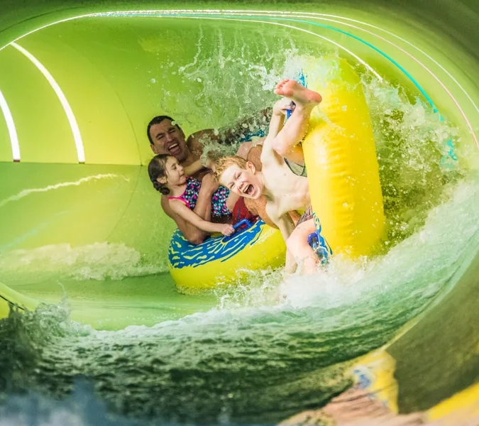 Två barn och en man åker tillsammans på badringar i en vattenrutschkana.