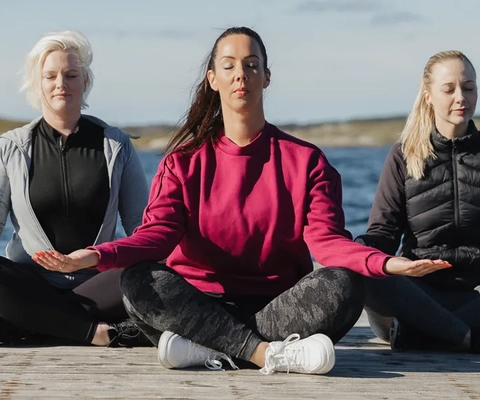 Tre kvinnor sitter på en brygga och gör yoga.