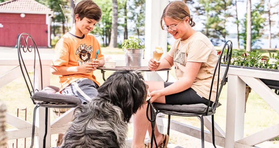 Barn äter glass med en hund vid sidan av bordet.