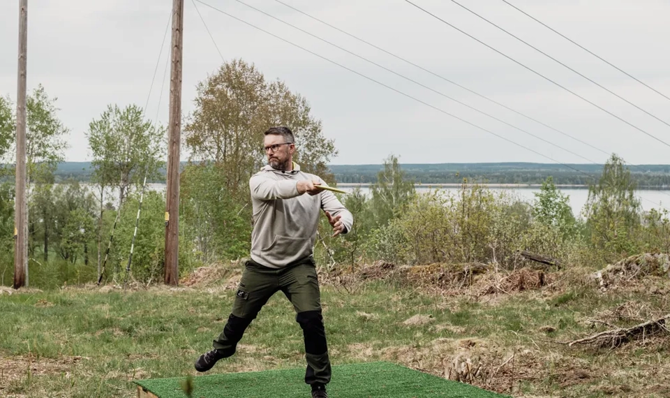 En discgolfspelare som tar sats för att kasta. i bakgrunden syns träd, en sjö och en kraftledning.