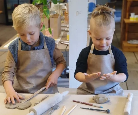 Två barn sitter och leker med lera i en keramikstudio.