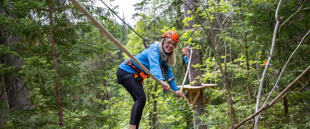 A woman is zipping through the trees on a zip line.