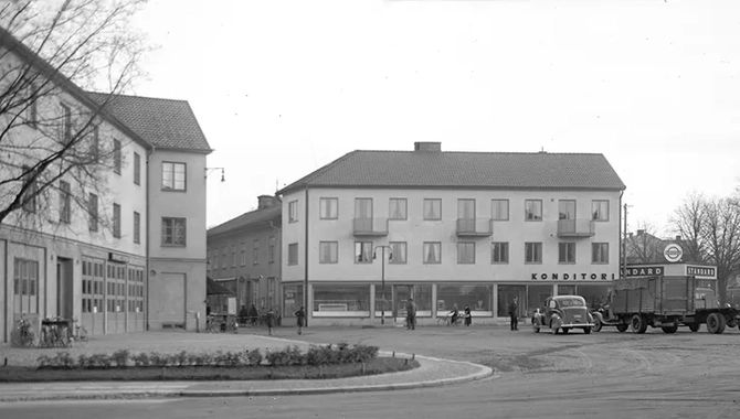 Ett stort torg med en gammal bil och några äldre vagnar. Byggnader i bakgrunden
