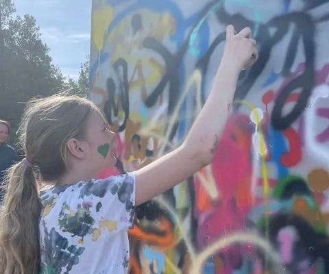 En ung flicka skriver på en vägg täckt av graffiti.